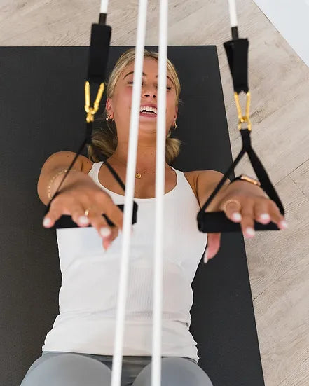 A person using a Pilates Mini consisting of a resistance band with gold links and handles, for a workout.