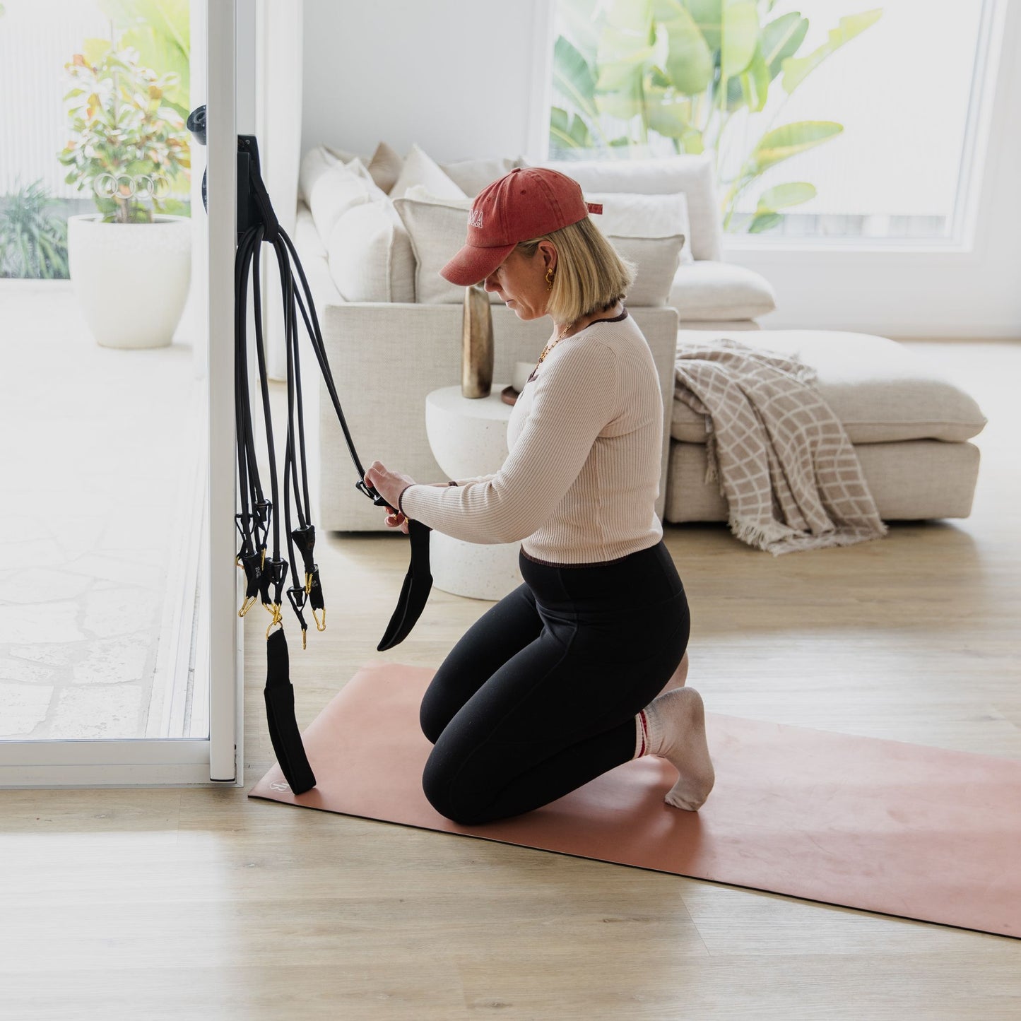 Woman exercising on a pink mat with black resistance bands in a living room.
