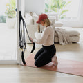 Woman exercising on a pink mat with resistance bands in a bright living room.