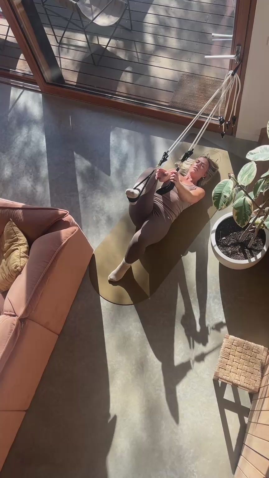 A woman is doing Pilates reformer exercises using white Pilates Mini Travel Kit resistance bands attached to a door in her home.