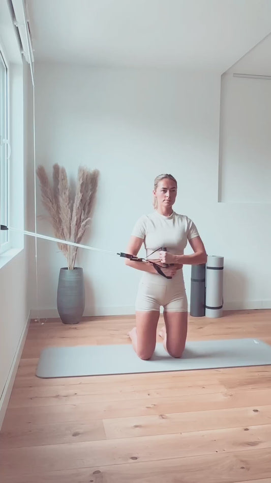 A woman is practicing an exercise movement by pulling her arms using a Pilates Mini resistance band.